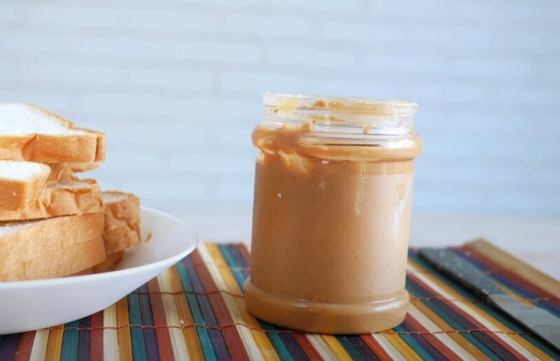 A jar of peanut butter with a plate of bread next to it