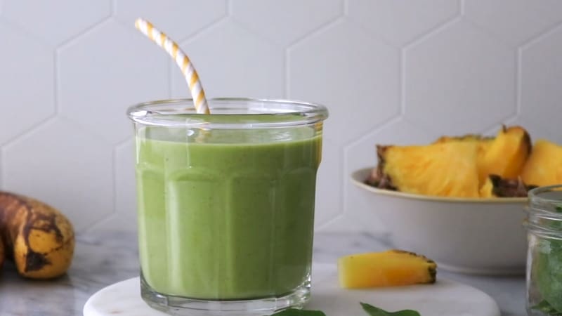 Green smoothie in a glass with a straw, next to banana and pineapple
